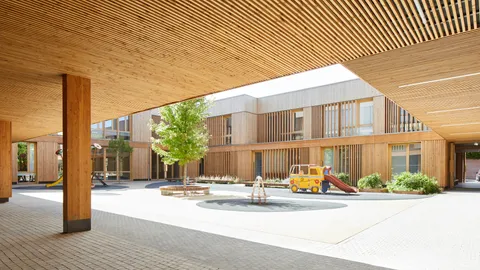Cours d'école ensoleillée entouré de bâtiments recouverts de tasseaux claire-voie